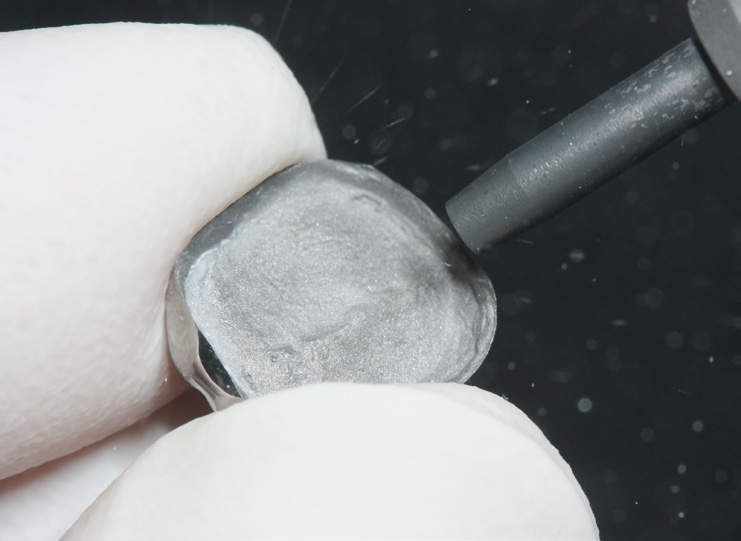 A close-up of a hand polishing a rough gemstone with a rotary tool.