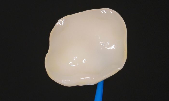 Close-up of a smooth, irregularly shaped white dental crown held by a blue tool against a black background
